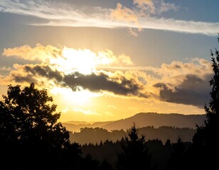 Golden sunset over layered mountains, framed by silhouetted trees