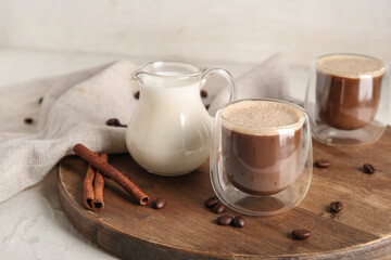 Glasses of hot coffee with cinnamon and jug of fresh milk on white background