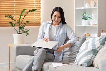Fototapeta premium Young woman with laptop sitting on sofa at home. Refund concept