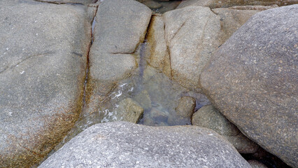 Clear sea water flowing through the gaps of giant granite rocks on the shore of Siangau Beach showcasing natural coastal geology