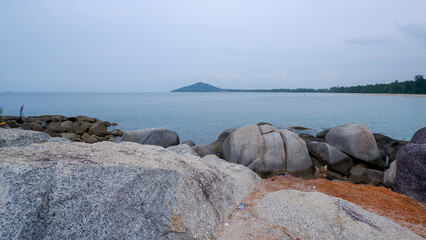 Beautiful seascape from Siangau Beach showing granite rocks in the foreground and a mountain or hill on the horizon across the sea