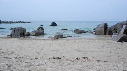 A calm dog resting on the white sand near giant granite boulders at Siangau Beach, Bangka Island, Indonesia