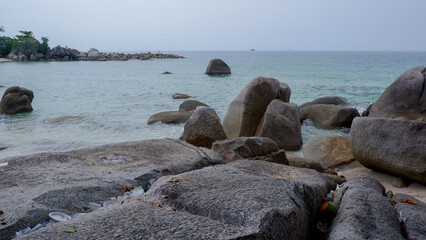 Environmental issue showing plastic waste and litter trapped between granite rocks at Siangau Beach, Bangka, Indonesia