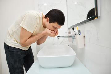 Man rinsing after brushing teeth over sink in modern bathroom