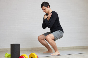 Man performing a bodyweight squat on a yoga mat during a training session at home