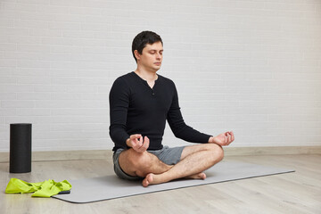 Man sitting in lotus pose on grey mat, meditating with eyes closed and hands in mudra