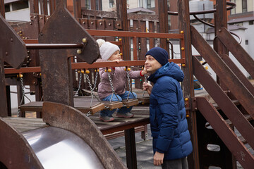 Caring dad assisting child enjoying outdoor play on urban playground in winter