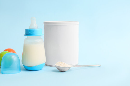 Feeding bottle with baby milk formula and rattle on color background