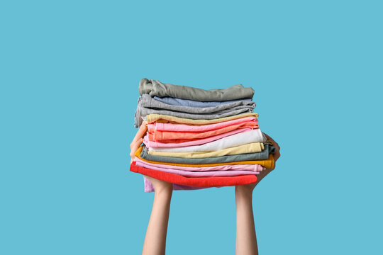 Female hands with stack of different clothes on blue background