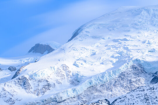 Expansive snowfields and jagged glacier formations cover the slopes of Mont Blanc, illuminated by soft daylight beneath a clear blue sky for a crisp alpine scene.