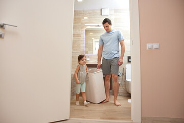 Father and daughter placing dirty clothes into a laundry hamper at home