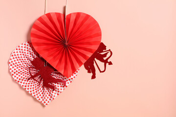 Naklejka premium Happy Valentine's Day concept. Hanging paper hearts and Cupid silhouettes on a soft pink background for Valentine's Day.