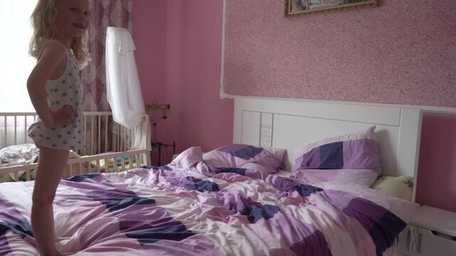 a little girl in slow motion jumps on a bed, carefree childhood of a child, playing on a bed