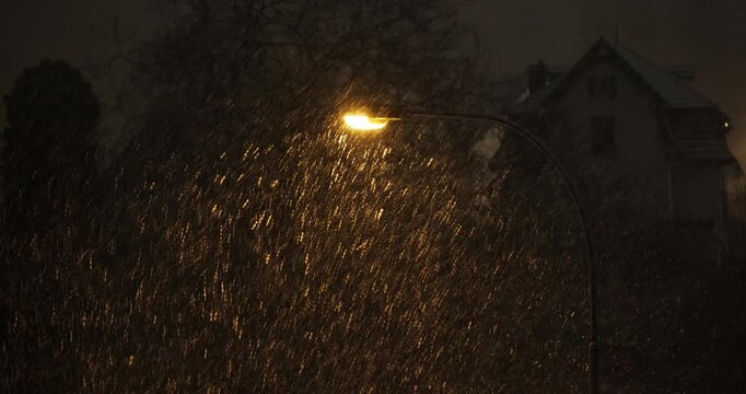 Street light illuminating falling snow during snowstorm at night. Above, wide angle view, real time video, dark background, no people