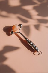 Fototapeta premium Metal facial massager with a peach-colored stone ball at the end on a soft peach background. Concept Metal Facial Massager, Peach Stone Ball, Soft Peach Background, Skincare Tool, Beauty Routine