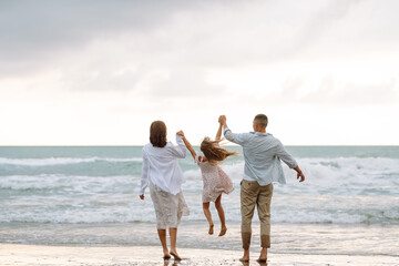 Young family with baby expecting baby strolls along the beach on a cloudy day. Happy man and a pregnant woman with their daughter enjoy time together and look at seascape. Concept of family and love.