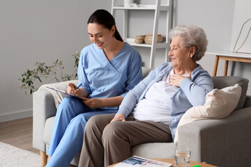 Obraz premium Senior woman with physical therapist writing in clipboard on sofa at home