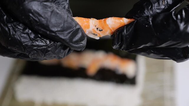 Close-up of a chef wearing gloves peeling and cracking a shrimp in a restaurant kitchen. The process of cooking Japanese dishes.