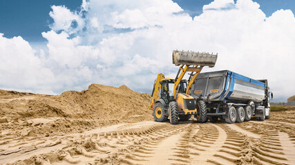 Fototapeta premium Deep tracks from heavy machinery cut through sandy ground with a large sand pile in the background showing ongoing construction activity
