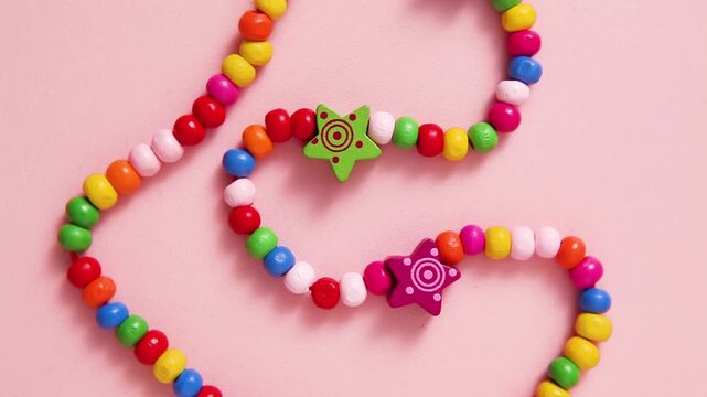 A colourful handmade beaded necklace featuring bright rainbow beads with cute star, rotating with soft pink background