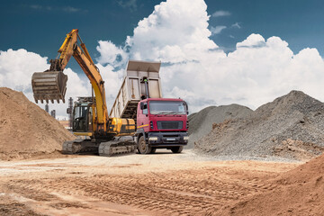 Obraz premium A backhoe loader moves sand into a truck at a busy construction site. This modern equipment is essential for efficiently handling large volumes of material