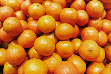 Fresh mandarins are piled high in a market. Shoppers are browsing the selection of fruits. The...