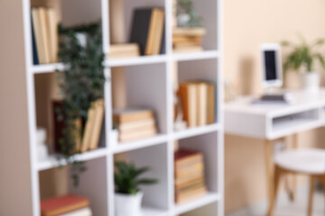 Fototapeta premium Interior of modern living room with workplace and bookshelf near beige wall, blurred view