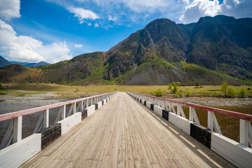 Wooden bridge over Chulyshman river in Altai Russia leading into scenic mountain valley Perspective view into remote wilderness