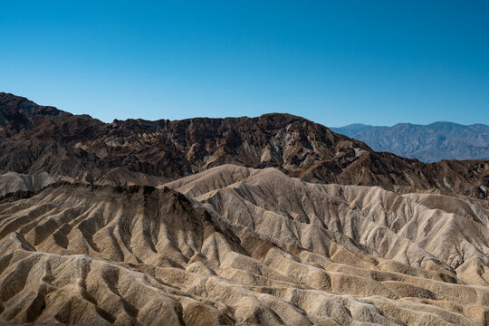 A stunning panoramic view of Death Valley, showcasing vast, arid desert landscapes with rugged mountains and golden sand dunes stretching into the horizon under a clear blue sky.