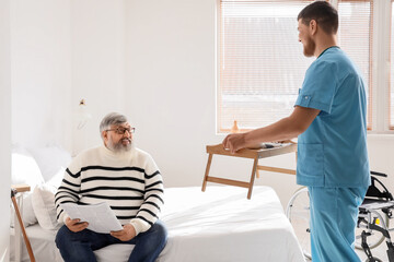 Obraz premium Senior man with newspaper receiving breakfast from caregiver in bedroom