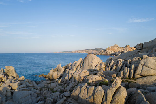 Weathered granite formations overlook the calm blue waters of the Mediterranean Sea at Capo Testa, Sardinia, under a clear sky with soft natural light.