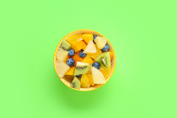 Bowl with fresh fruit salad on green background