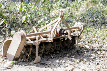 unused rotary tiller farm implement resting outdoors, showing worn metal blades and agricultural machinery details