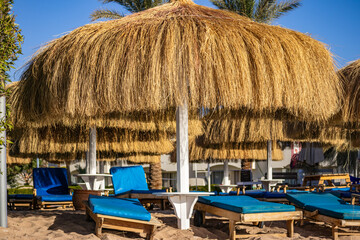 Empty beach loungers under straw umbrellas on a sunny seaside resort. Concept of vacation