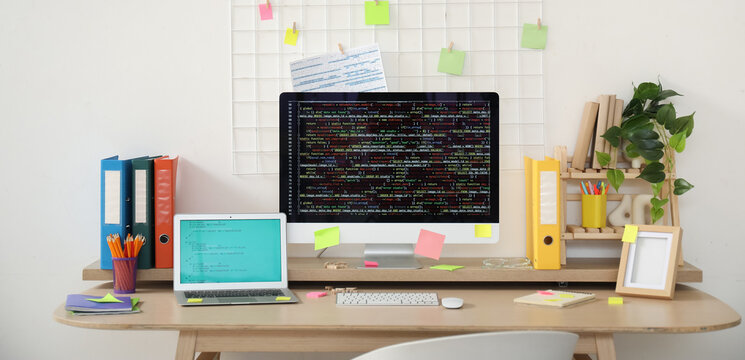 Computer monitor and laptop with codes on programmer's desk in light office