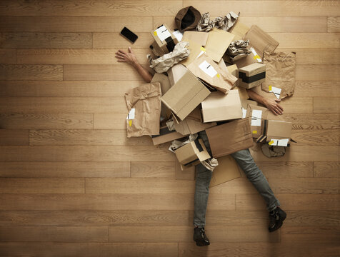Exhausted man submerged by empty boxes, concept of excessive consumerism and compulsive online shopping