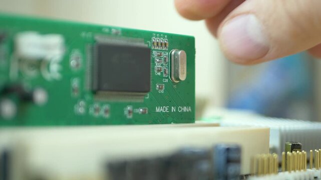PC repair master inserts PCI board into motherboard area. Green PCB with Made in China note. Electronic circuit card background. Computer repair and maintenance workshop