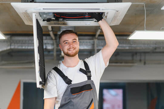 Technician maintaining ceiling air conditioning system smiling