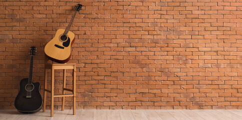 Different guitars on chair near brown brick wall