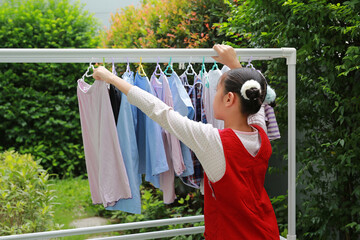Asian girl hanging the laundry on a clothes rail at the garden near house.