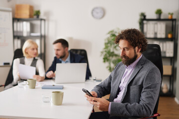 A business team works in a meeting room discussing ideas and plans for success. One member checks their phone while others collaborate at the table.