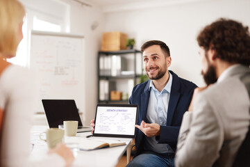 Fototapeta premium Team members share ideas and insights on a growth strategy. One person shows a chart on a tablet while others listen attentively in a modern office environment.