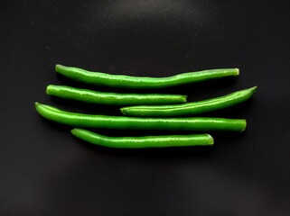 Fresh Green Beans on Dark Background. The image shows five green beans placed horizontally against...