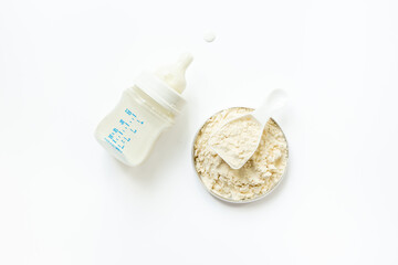Powdered infant formula in jar lid and scoop with baby milk bottle on white background. Top view.