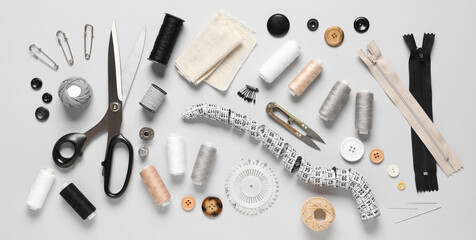 Set of thread spools with fabric, measuring tape, scissors and sewing supplies on grey background