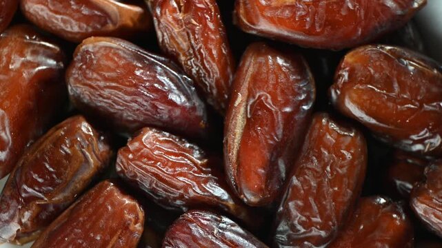 Premium quality dried Medjool dates rotating slowly on a deep black background. Glossy brown skin, wrinkled texture, natural sweetness. Fresh organic dried fruit, healthy snack concept. Smooth 360-deg