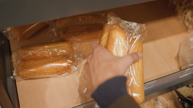 Worker packing wrapped rolls on shelf, gloved hands selecting packaged bread for grocery order, smartphone visible for scanning, warm bakery lighting, plasticwrapped rolls arranged in drawer ready