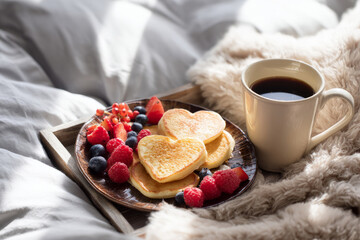 Valentine's cozy breakfast in bed with heart-shaped pancakes, coffee, and fresh berries, soft morning sunlight, inviting lifestyle stock photography