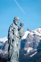 Statue of Saint Joseph holding baby Jesus before winter mountain landscape.