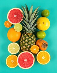 A vibrant tropical fruit arrangement with a mix of citrus fruits, pineapples, and limes on a teal background